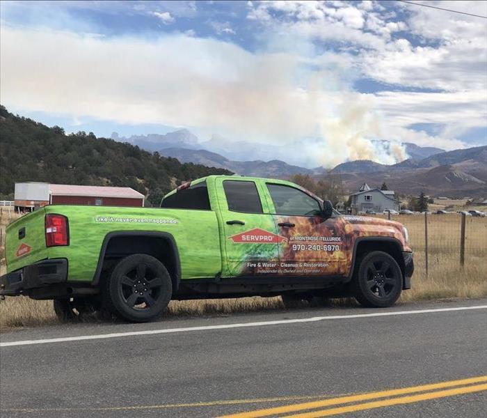 SERVPRO vehicle parked on side of country road with a house and further in the background smoke raining up from the hills and
