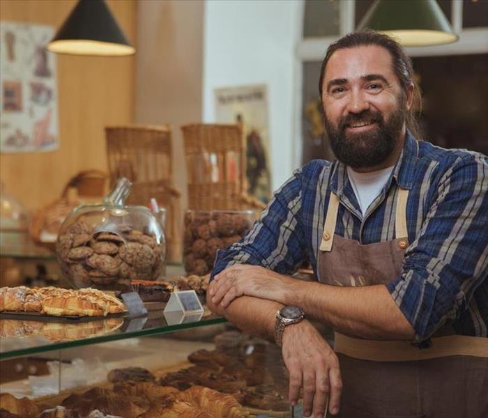 A man with a brown apron on in a bakery. 
